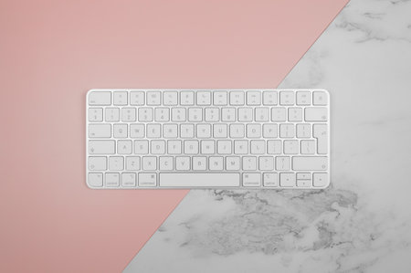 Top view of white keyboard on pink and white marble background. Modern office flat lay, copy space.