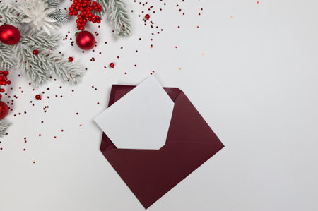 Christmas composition, red envelope, fir tree branches, red berries, baubles and stars confetti on...