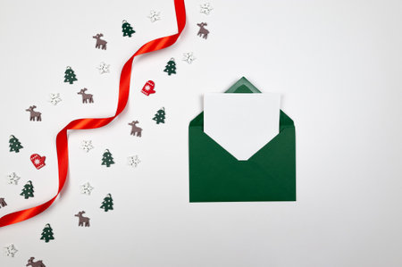 Christmas composition, green envelope, white card, red ribbon and confetti on white background. Shiny rolled fabric, silk and satin material. Top view, flat lay, copy space.の写真素材