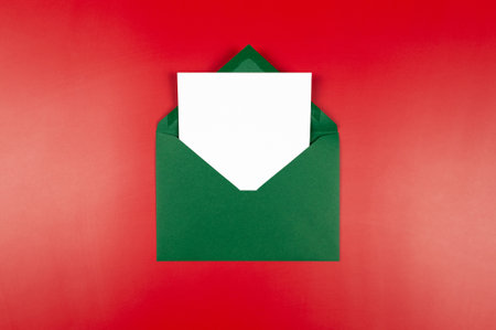 Top view of green envelope, white card on red background. Christmas, New Year composition. Post flat lay, copy space.の写真素材