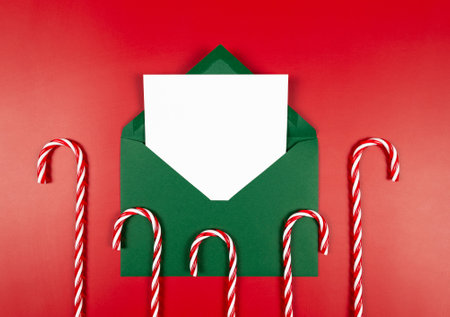 Top view of green envelope, white card and candy canes on red background. Christmas, New Year...