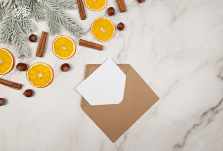 Christmas composition, dried orange slices, fir tree branches, cinnamon sticks, hazelnuts on white marble background. Kraft envelope, white card. Top view, flat lay, copy space.の写真素材