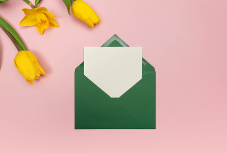 Top view of yellow tulips and daffodils on pink background. Green envelope, white card. Spring colourful composition, flat lay, copy space.の写真素材