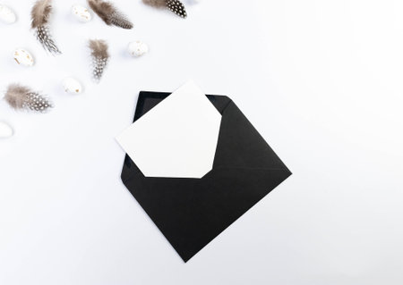 Top view of brown feathers, white easter eggs, black envelope and white card on white background. Creative easter composition, spring, copy space, flat lay.の写真素材
