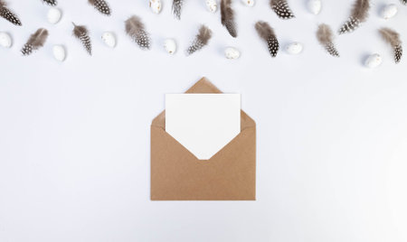 Top view of brown feathers, white easter eggs, kraft envelope and white card on white background. Creative easter composition, spring, copy space, flat lay.の写真素材