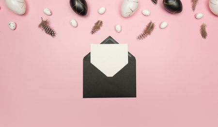 Top view of easter eggs, feathers, black envelope and white card on pink background. Creative easter...