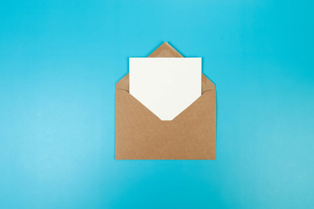 Top view of brown Kraft envelope, white card on blue background. Post flat lay. Copy space.の写真素材
