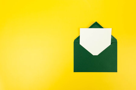 Top view of dark green envelope, white card on yellow background. Post flat lay. Copy space.の写真素材