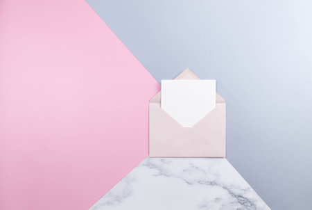 Top view of light pink envelope, white card on colourful background. Blue, pink and marble...