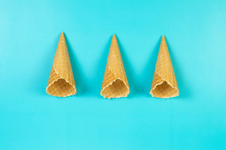 Top view of three ice cream waffle cones on blue background. Summer wallpaper, flat lay, copy space.の写真素材