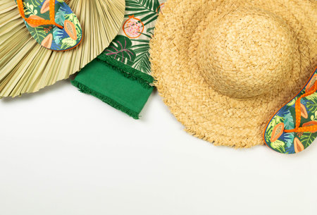 Top view of straw hat, slippers, dried palm leaf and green towels on white background. Summer...