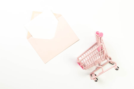 Top view of pink shopping trolley on white background. Pink envelope, white card, post. Creative shopping wallpaper, sale. Copy space, flat lay.の写真素材