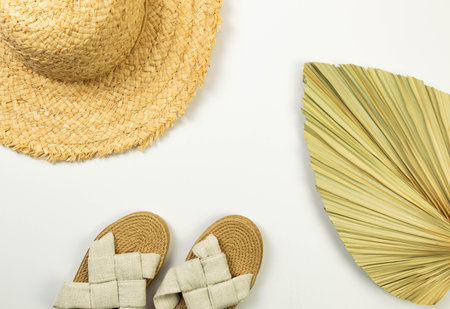 Top view of straw hat, slippers and dried palm leaf on white background. Summer fashion, vacation and beach wallpaper. Copy space, flat lay.の写真素材