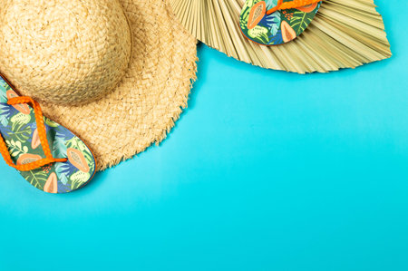 Top view of straw hat, dried palm leaf and slippers on blue background. Summer fashion, vacation and beach wallpaper. Copy space, flat lay.の写真素材
