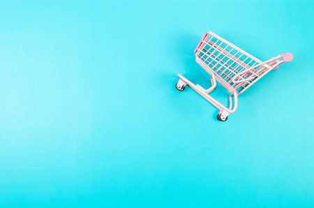 Top view of pink shopping trolley on blue background. Creative shopping wallpaper, sale. Copy space, flat lay.の写真素材