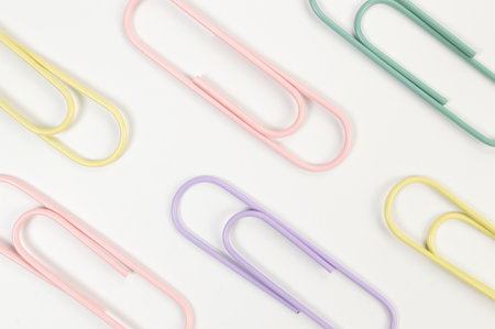 Top view of colorful paperclips on white background. School, office wallpaper. Flat lay, copy space.
