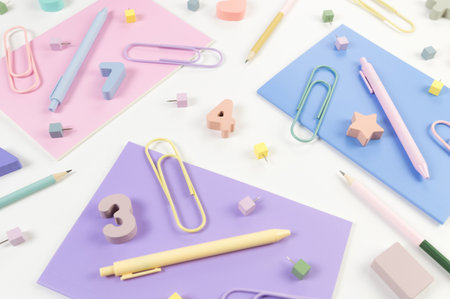 Top view of pink, purple and blue notebooks on white background. Colorful pens, pencils, paperclips,...