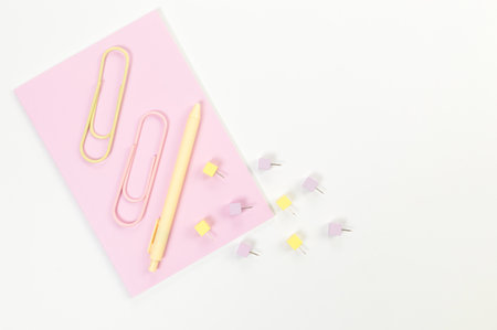 Top view of pink notebook on white background. Paperclips, pen and pins. School, office wallpaper. Flat lay, copy space.の写真素材