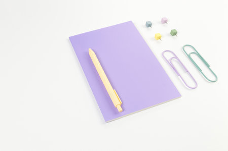 Top view of purple notebook on white background. Paperclips, pen and pins. School, office wallpaper....