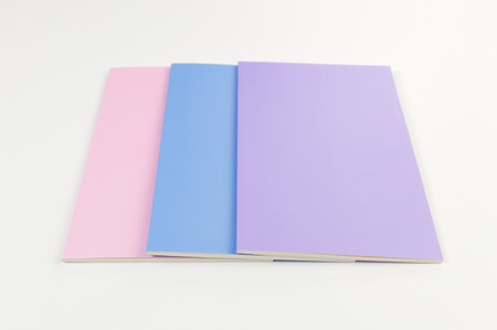 Top view of pink, purple and blue notebooks on white background. School, office wallpaper. Flat lay,...