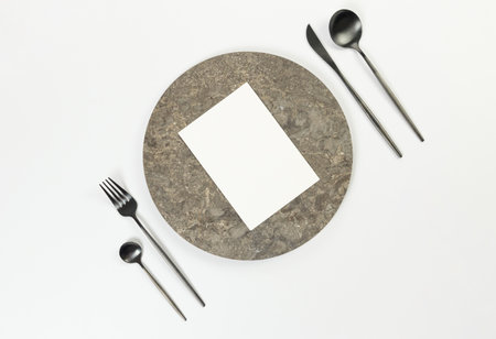 Top view of brown marble plate, black cutlery and white card on white background. Food presentation, stone tray. Table setting, copy space, flat lay.の写真素材