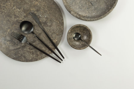 Top view of brown marble tray, plate, bowl and black cutlery on white background. Food presentation, dishes, stone tray. Copy space, flat lay.の写真素材