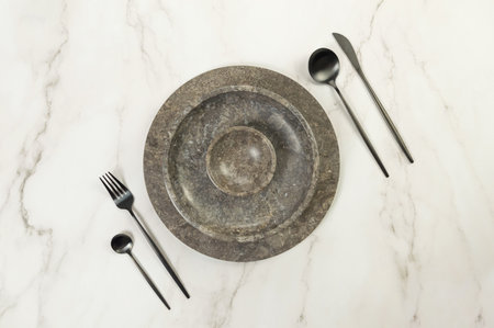 Top view of brown marble tray and plate, black cutlery on white marble background. Food presentation, stone tray. Table setting, copy space, flat lay.の写真素材