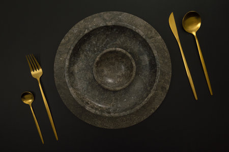 Top view of brown marble tray and plate, gold cutlery on black background. Food presentation, stone tray. Table setting, copy space, flat lay.の写真素材