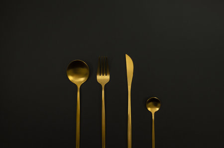Top view of gold cutlery on black background. Knife, fork, spoon and dessert spoon. Copy space, flat...