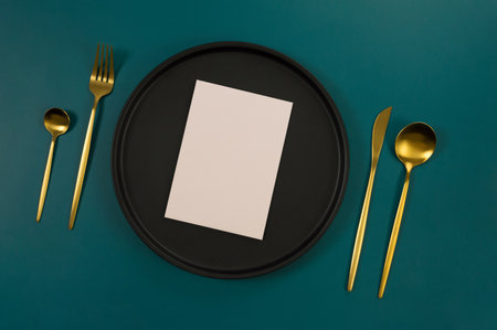 Top view of black plate, gold cutlery and pink card on dark green background. Food presentation, black tray. Table setting, copy space, flat lay.の写真素材
