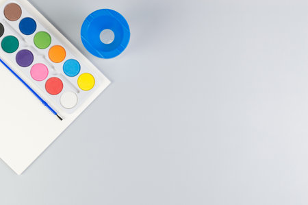 Top view of watercolor, paper, water pot and paint brush on grey background. Painting, art, copy space, flat lay.の写真素材
