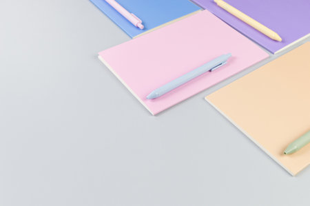 Top view of pink, purple, blue and beige notebooks on grey background. Colorful pens, school, office...
