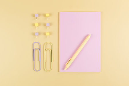 Top view of pink notebook on yellow background. Paperclips, pen and pins. School, office wallpaper....
