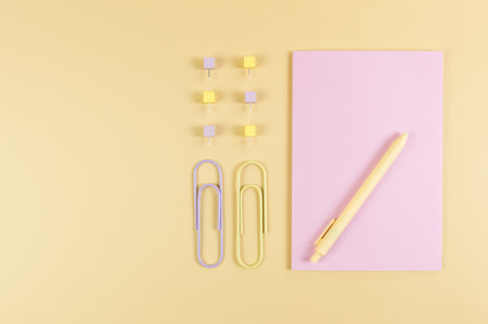 Top view of pink notebook on yellow background. Paperclips, pen and pins. School, office wallpaper....