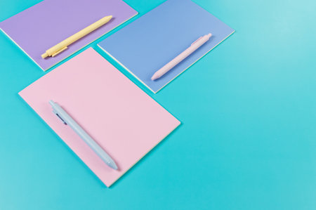 Top view of pink, purple and blue notebooks on blue background. Pink, yellow and blue pens, school, office wallpaper. Flat lay, copy space.の写真素材