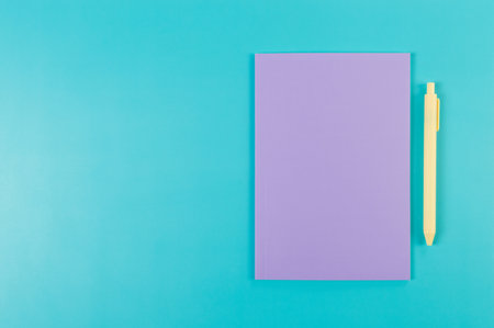 Top view of purple notebook, yellow pen on blue background. School, office wallpaper. Flat lay, copy space.の写真素材