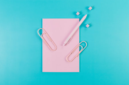 Top view of pink notebook on blue background. Paperclips, pen and pins. School, office wallpaper. Flat lay, copy space.の写真素材
