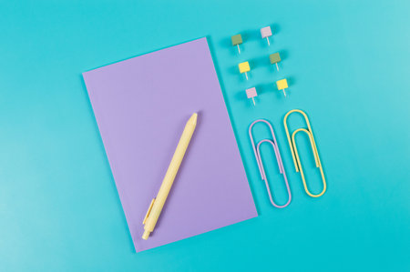 Top view of purple notebook on blue background. Paperclips, pen and pins. School, office wallpaper....