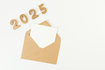 2025 Happy New Year. Top view of gold numbers, brown kraft envelope, white card on white background. Copy space, flat lay.の写真素材