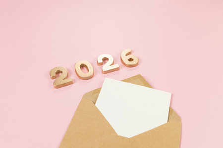 2026 Happy New Year. Top view of gold numbers, brown kraft envelope, white card on pink background. Copy space, flat lay.の写真素材