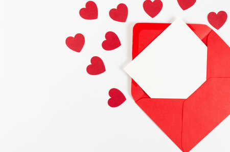 Top view of red envelope, white card on white background. Valentine's day, red hearts, love. Post...