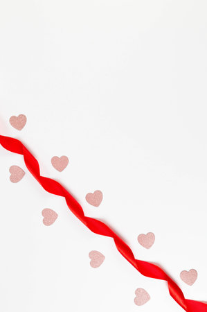 Top view of red ribbon and pink glitter hearts on white background. Valentine's day, love. Shiny rolled fabric, silk and satin material. Copy space, flat lay.の写真素材