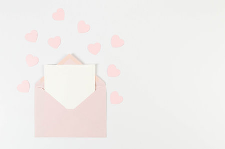 Top view of pink envelope, white card on white background. Valentine's day, pink hearts, love. Post...