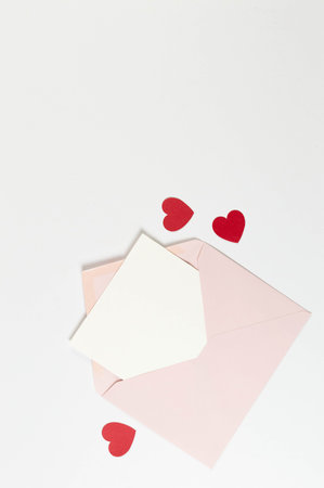 Top view of pink envelope, white card on white background. Valentine's day, red hearts, love. Post flat lay, copy space.の写真素材