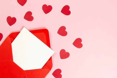 Top view of red envelope, white card on pink background. Valentine's day, red hearts, love. Post...