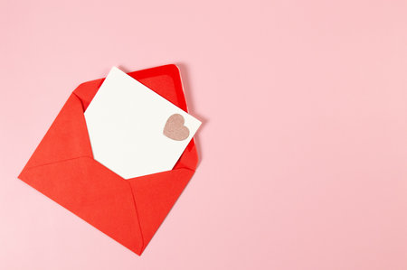Top view of red envelope, white card on pink background. Valentine's day, pink glitter heart, love. Post flat lay, copy space.の写真素材
