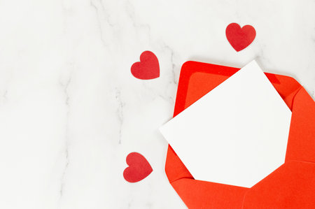 Top view of red envelope, white card on white marble background. Valentine's day, red hearts, love....