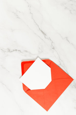 Top view of red envelope, white card on white marble background. Post flat lay. Copy space.
