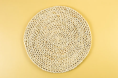 Top view of brown wicker table mat on yellow background. Straw round tray, flat lay, copy space.