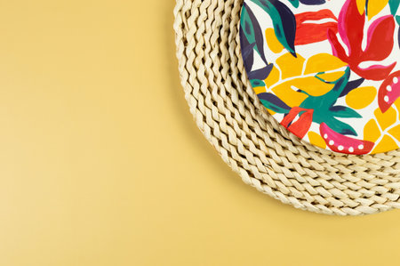 Top view of brown wicker table mat, colorful plate on yellow background. Straw round tray, exotic...